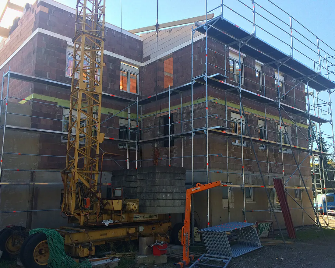Mehrstöckiges Gebäude im Rohbau mit Gerüst und Baukran auf der Baustelle