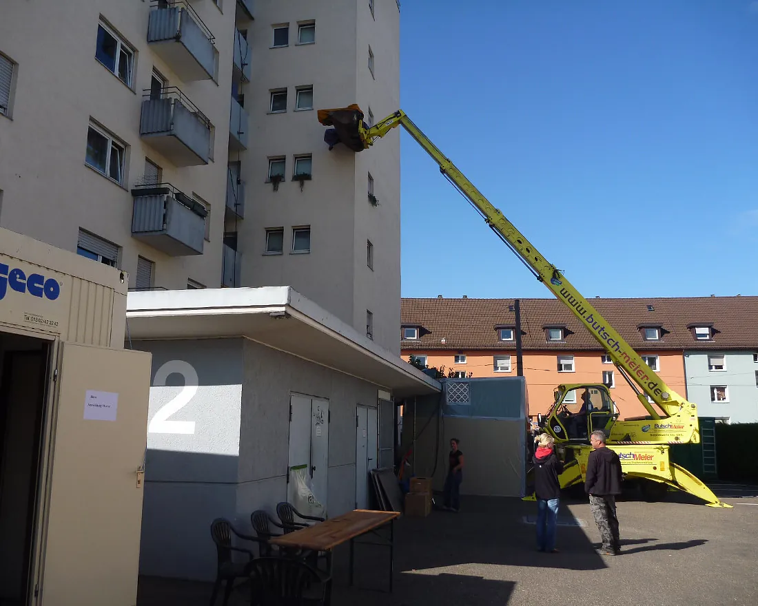 Gelber Teleskoplader hebt Arbeiter an der Fassade eines mehrstöckigen Wohngebäudes mit Brandschaden