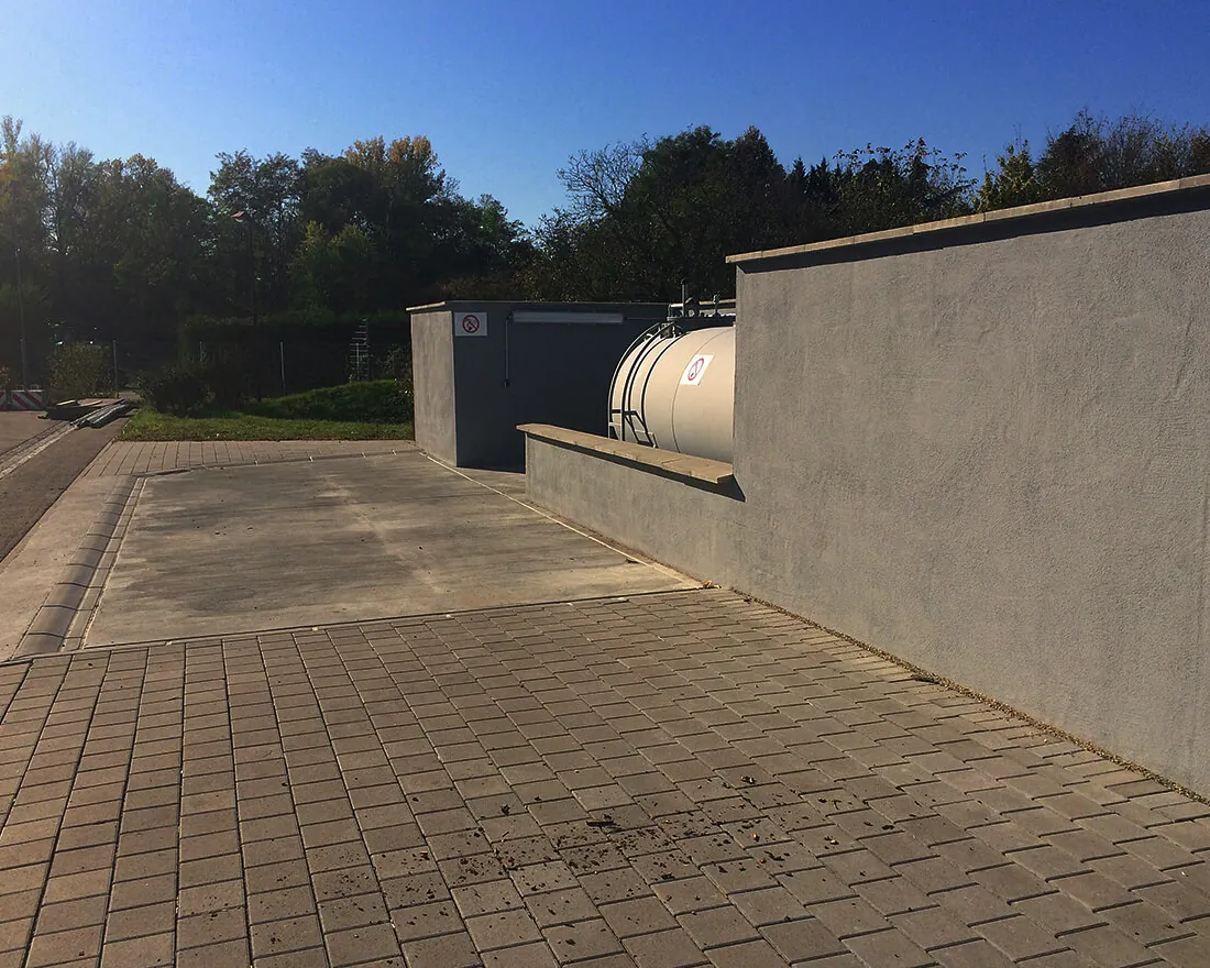 Außenbereich einer Tankstelle mit grauem Tank und Umzäunung aus Betonmauern unter blauem Himmel