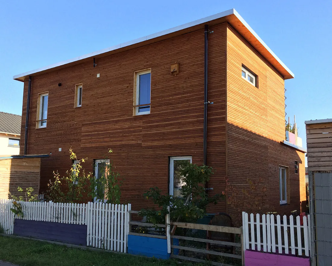 Modernes zweistöckiges Einfamilienhaus aus Holz mit mehreren Fenstern und weißem Lattenzaun im Garten