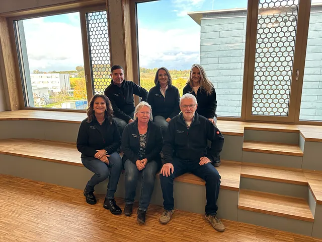 Sechs Personen sitzen auf einer modernen Holztreppe