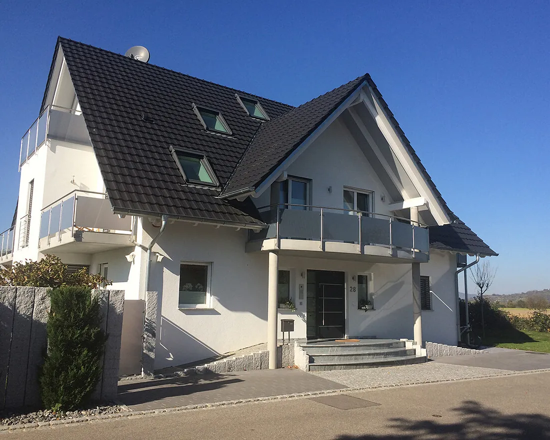 Zweifamilienhaus mit weißer Fassade, dunklem Satteldach und Balkon über dem Eingang
