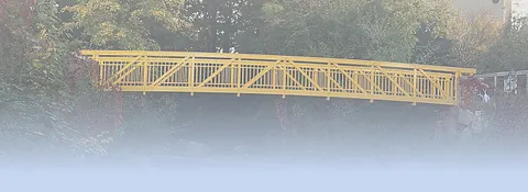 Gelbe Stahlbrücke über einem Fluss, umgeben von Bäumen mit herbstlichem Laub