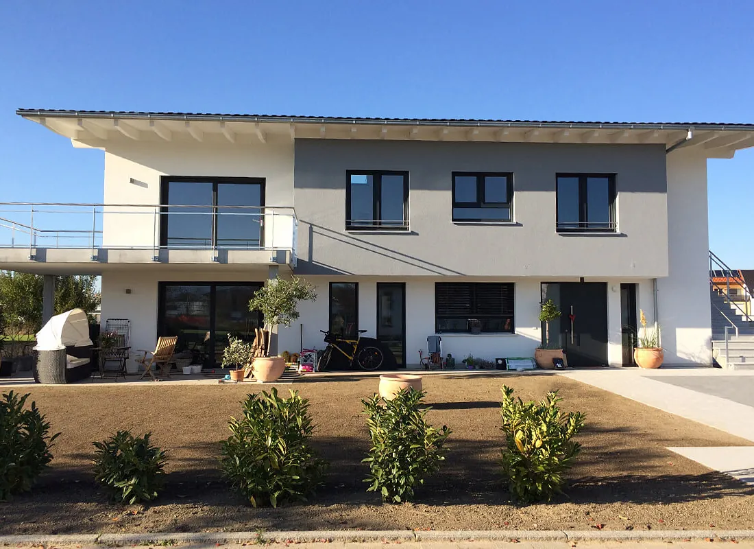 Modernes zweistöckiges Zweifamilienhaus mit Balkon, großen Fenstern und Garten mit Sträuchern